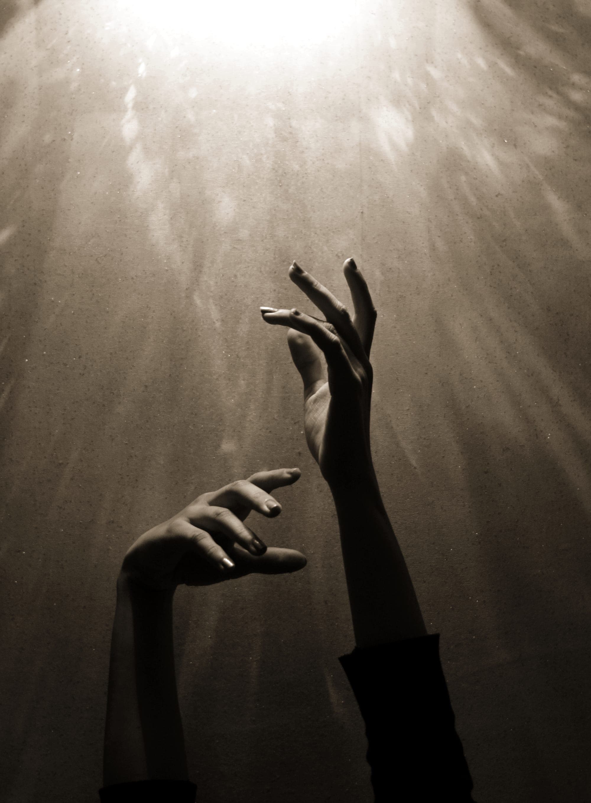 Two hands reaching up into a shaft of light