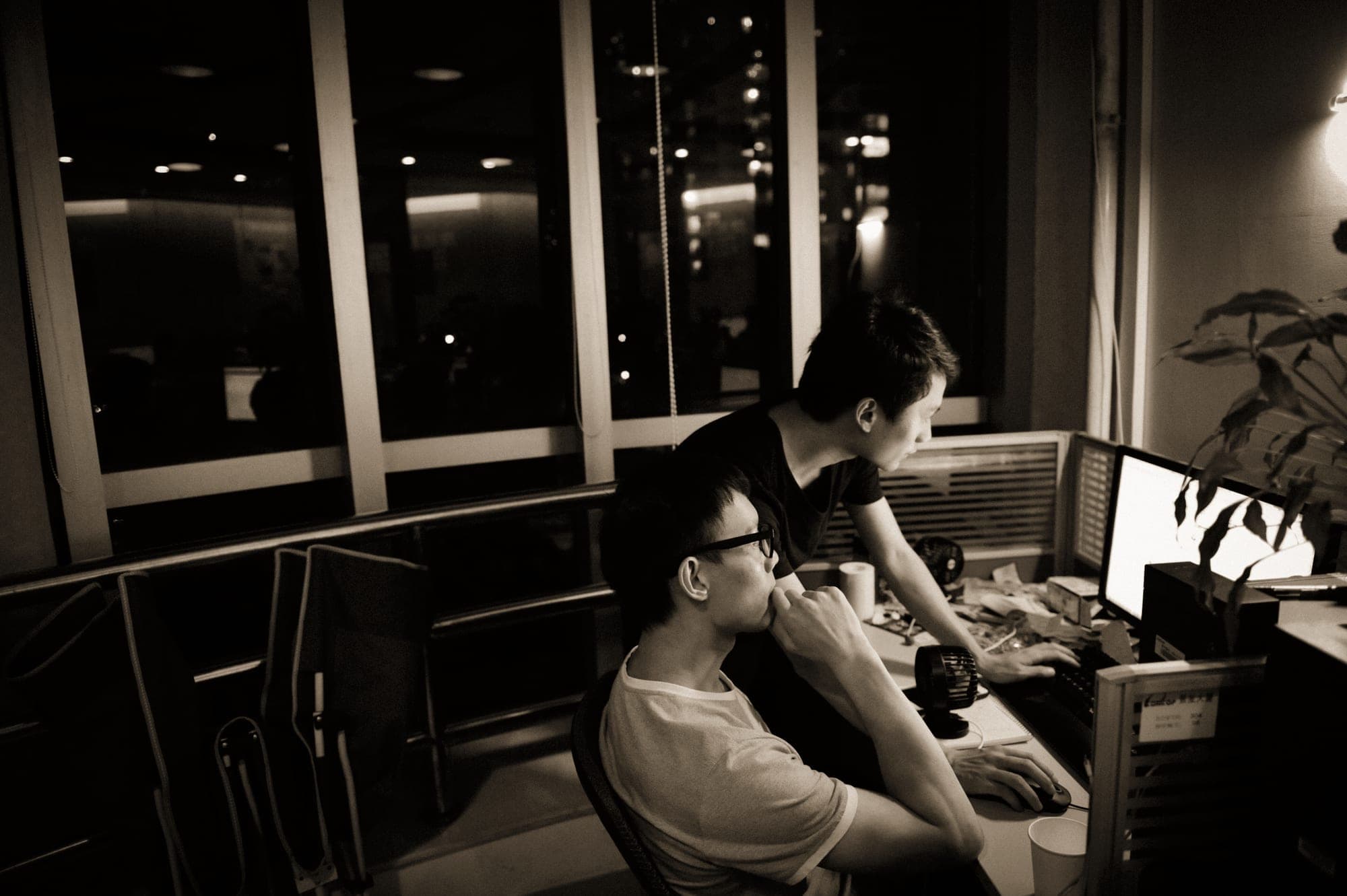 Two people at a desk at night, one walking the other through something on screen